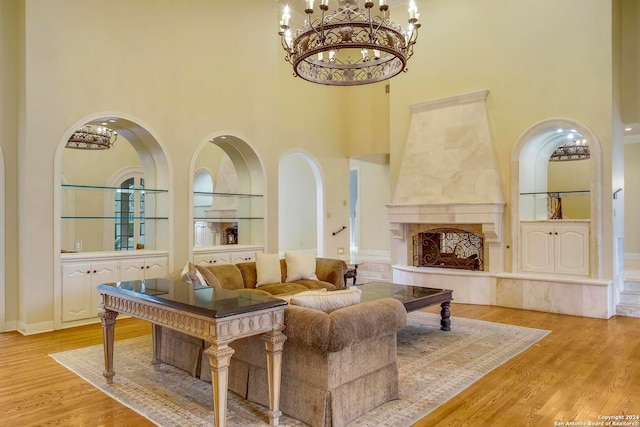 living room with a high end fireplace, light wood-type flooring, a chandelier, and a high ceiling