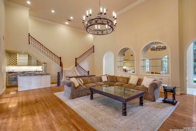 living room featuring an inviting chandelier, light hardwood / wood-style flooring, beverage cooler, ornamental molding, and a high ceiling