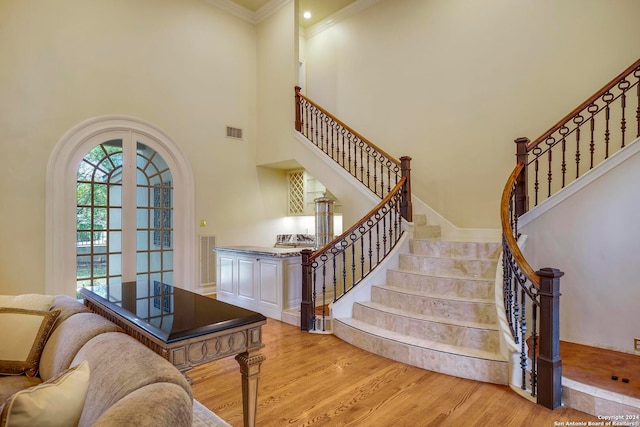 stairs with a towering ceiling, wood-type flooring, and ornamental molding