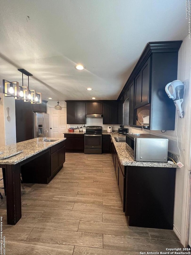 kitchen with an island with sink, light wood-type flooring, light stone countertops, and appliances with stainless steel finishes