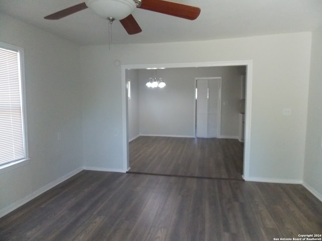 unfurnished room featuring ceiling fan with notable chandelier, a wealth of natural light, and dark hardwood / wood-style floors