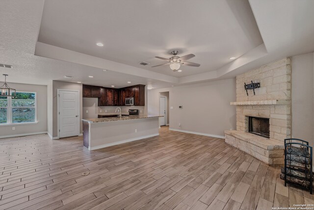 unfurnished living room featuring a fireplace, light hardwood / wood-style floors, a raised ceiling, and ceiling fan