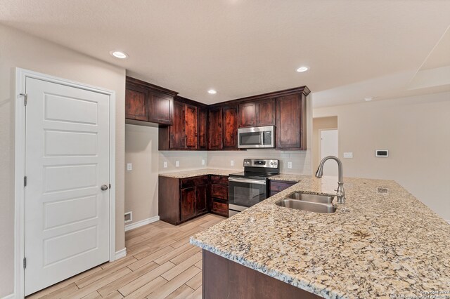 kitchen with light stone countertops, sink, kitchen peninsula, decorative backsplash, and appliances with stainless steel finishes