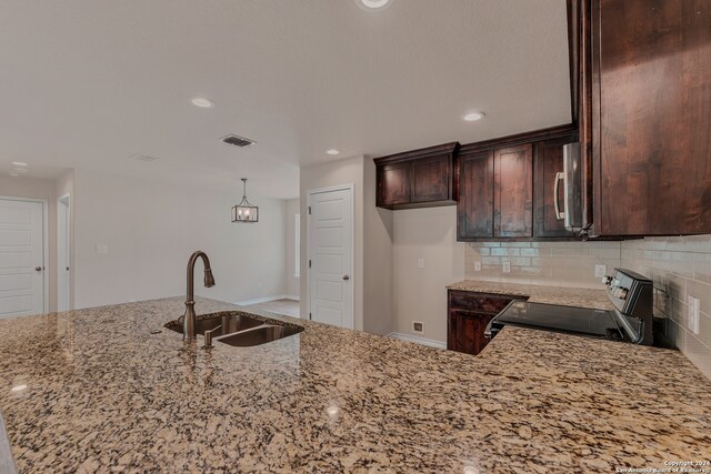 kitchen with appliances with stainless steel finishes, tasteful backsplash, light stone counters, sink, and decorative light fixtures