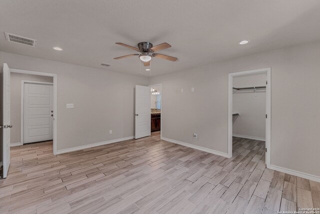 unfurnished bedroom featuring a walk in closet, a closet, light hardwood / wood-style flooring, and ceiling fan