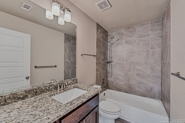 full bathroom featuring a textured ceiling, vanity, toilet, and tiled shower / bath