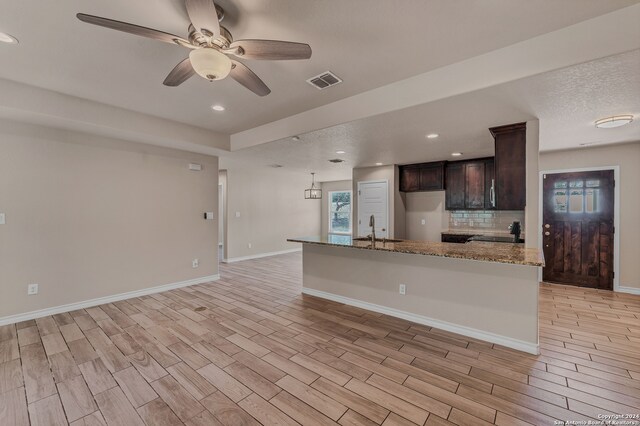 kitchen featuring light stone countertops, tasteful backsplash, dark brown cabinets, ceiling fan with notable chandelier, and sink