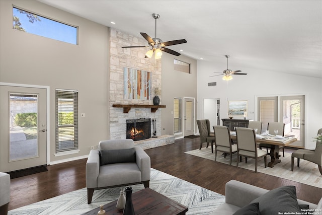 living room with dark wood-type flooring, ceiling fan, a stone fireplace, and a healthy amount of sunlight