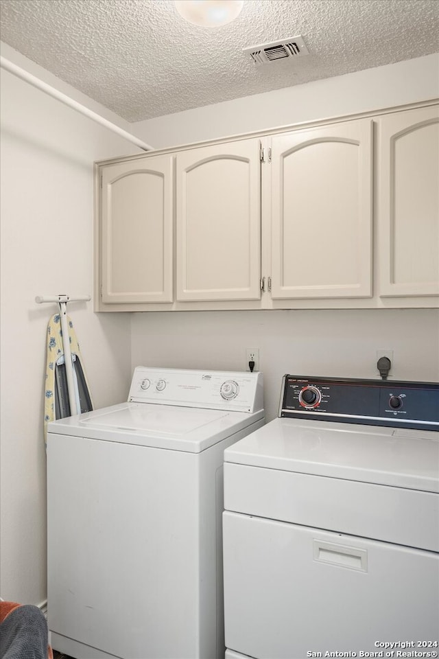 washroom featuring washing machine and clothes dryer, cabinets, and a textured ceiling