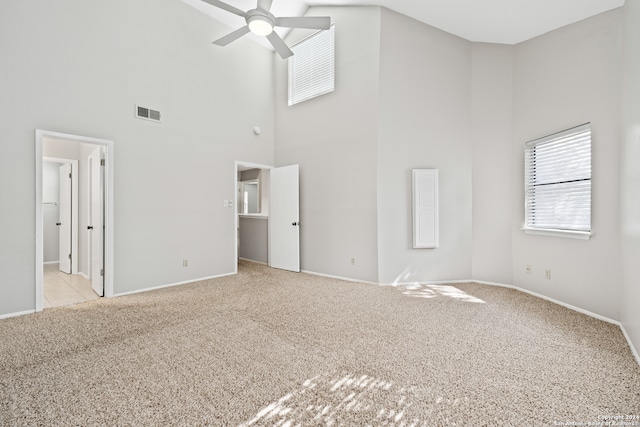 unfurnished living room with ceiling fan, light colored carpet, and a towering ceiling