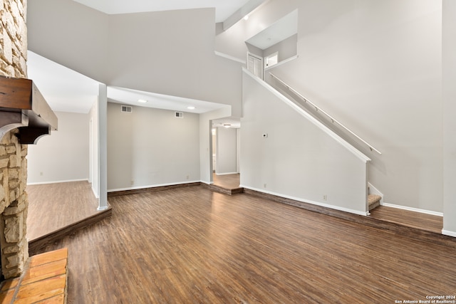 unfurnished living room with a stone fireplace, a high ceiling, and dark hardwood / wood-style floors