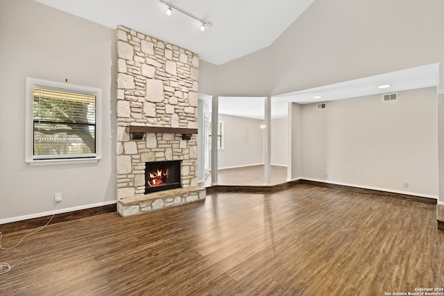 unfurnished living room featuring track lighting, hardwood / wood-style floors, high vaulted ceiling, and a stone fireplace