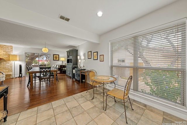 tiled dining space featuring brick wall and beamed ceiling