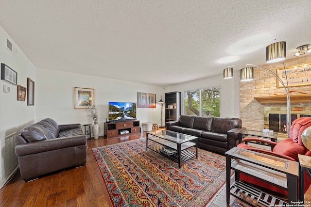 living room featuring dark hardwood / wood-style floors, brick wall, a textured ceiling, and a brick fireplace