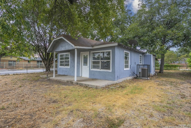 view of front of home featuring a patio, central air condition unit, fence, stucco siding, and a front lawn