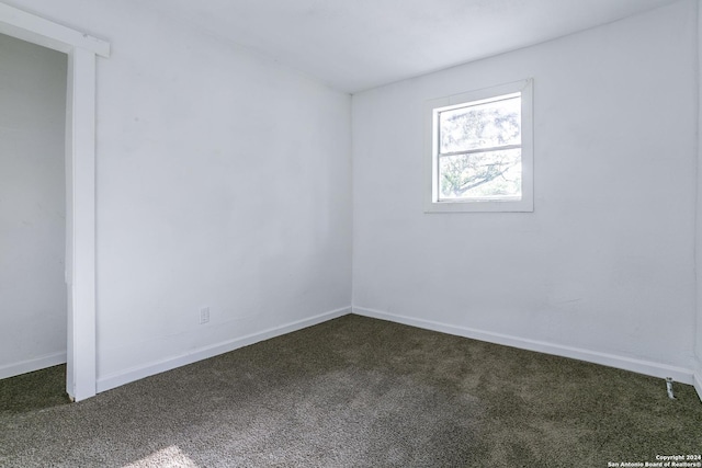 unfurnished room featuring dark carpet and baseboards