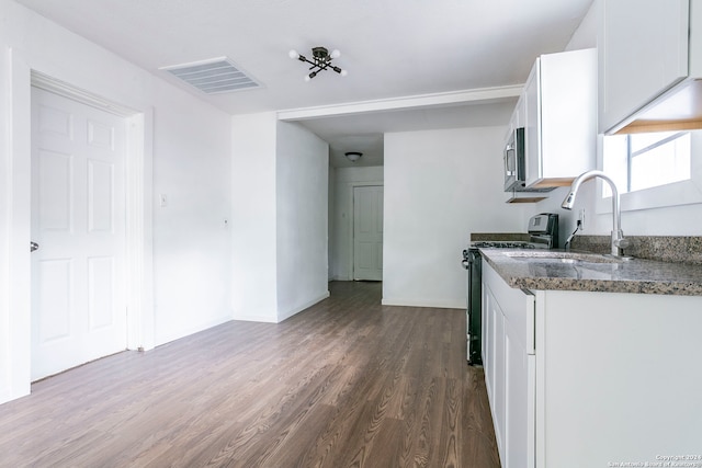 kitchen with dark stone countertops, stove, wood-type flooring, and white cabinetry