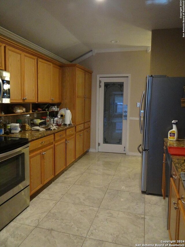 kitchen with light tile patterned floors, ornamental molding, stainless steel appliances, dark stone countertops, and vaulted ceiling