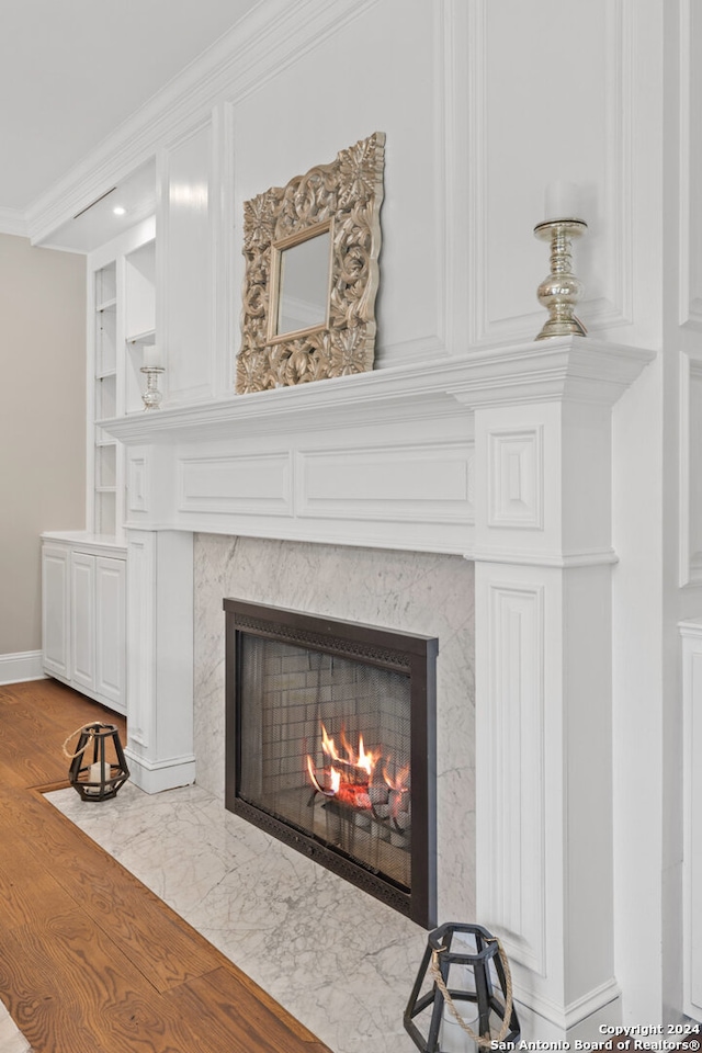 interior details with built in shelves, ornamental molding, hardwood / wood-style floors, and a high end fireplace