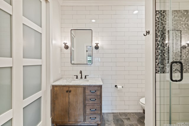 bathroom with tile walls, a shower with door, vanity, and toilet