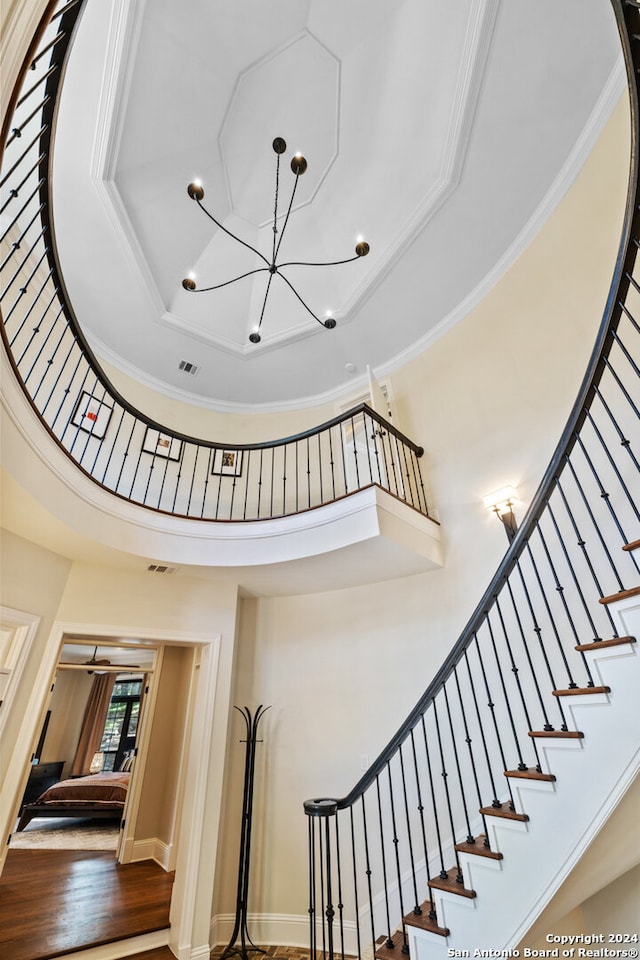 stairs with a towering ceiling, a tray ceiling, ornamental molding, hardwood / wood-style floors, and a notable chandelier