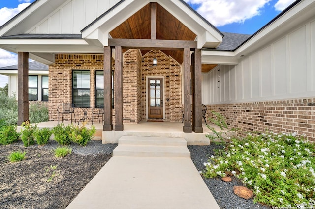 property entrance with roof with shingles, a porch, board and batten siding, and brick siding