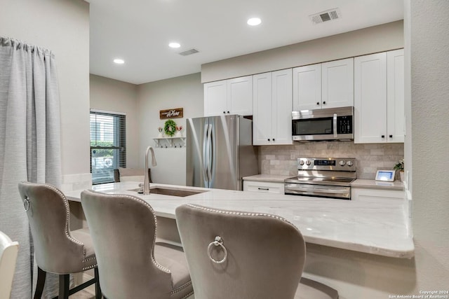 kitchen with light stone countertops, stainless steel appliances, white cabinetry, and sink