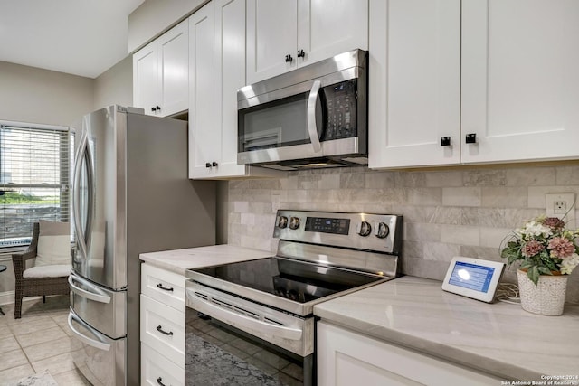 kitchen featuring light stone counters, light tile patterned floors, backsplash, appliances with stainless steel finishes, and white cabinetry