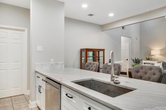 kitchen with light stone countertops, stainless steel dishwasher, sink, white cabinetry, and light tile patterned flooring