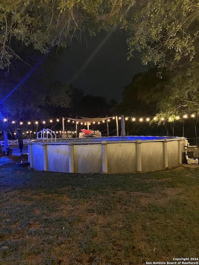 pool at night featuring a lawn