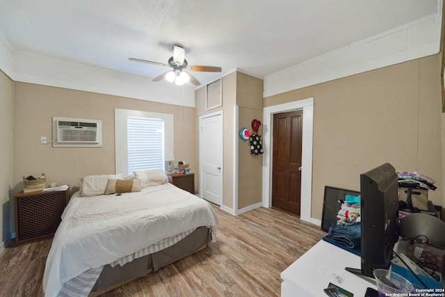 bedroom with a closet, a wall unit AC, hardwood / wood-style flooring, and ceiling fan