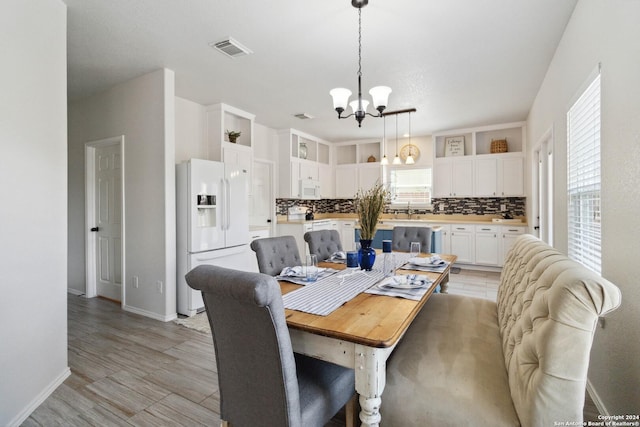 dining space featuring a chandelier, light wood finished floors, visible vents, and baseboards