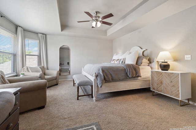 bedroom with arched walkways, a tray ceiling, carpet, and baseboards