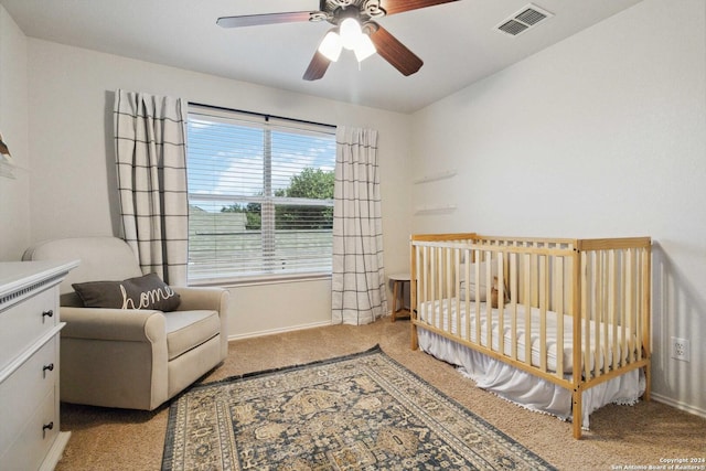 carpeted bedroom with a crib, visible vents, and a ceiling fan