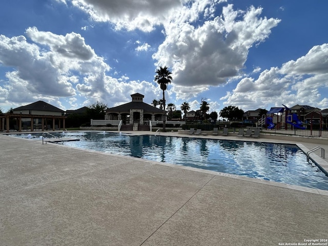 community pool featuring fence, playground community, and a patio