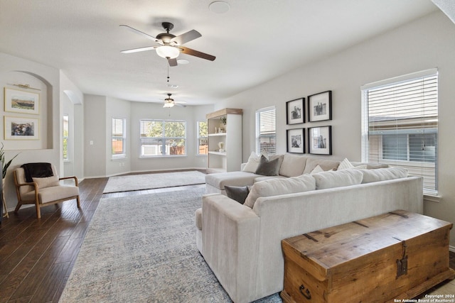 living room featuring arched walkways, dark wood finished floors, a ceiling fan, and baseboards