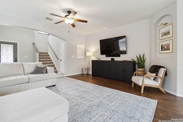 living room featuring ceiling fan, dark wood-style flooring, visible vents, baseboards, and stairway