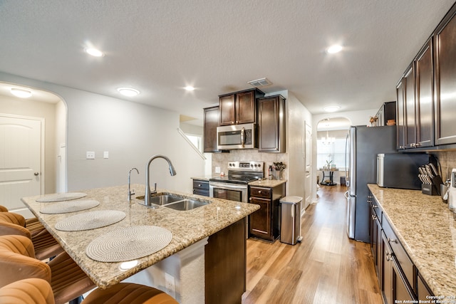 kitchen with appliances with stainless steel finishes, light hardwood / wood-style floors, sink, a breakfast bar area, and decorative backsplash