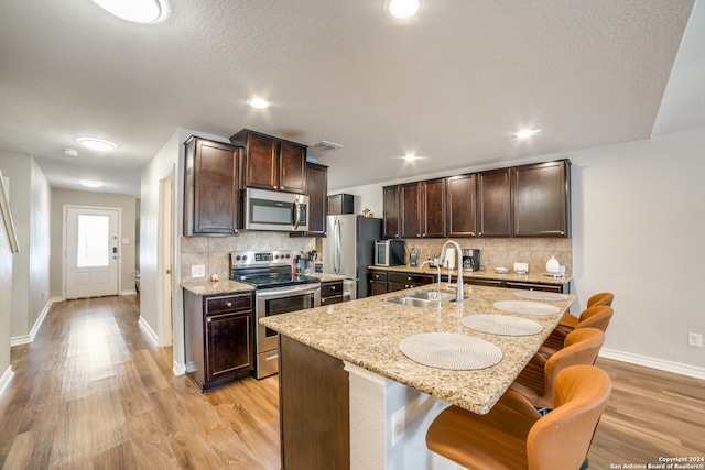 kitchen featuring a kitchen breakfast bar, appliances with stainless steel finishes, light hardwood / wood-style floors, an island with sink, and sink