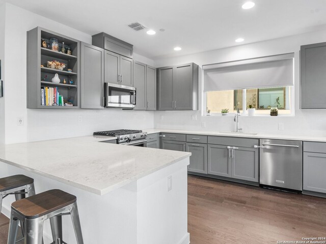 kitchen featuring tasteful backsplash, kitchen peninsula, sink, dark wood-type flooring, and appliances with stainless steel finishes