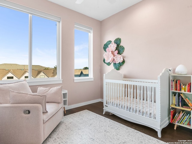 bedroom with hardwood / wood-style flooring, ceiling fan, multiple windows, and a crib