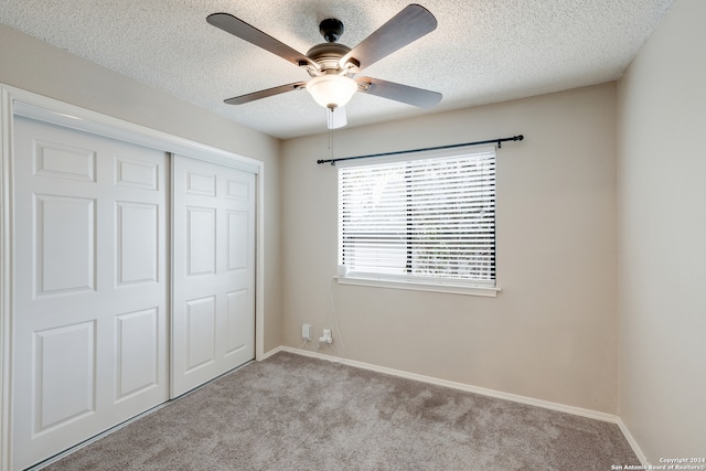 unfurnished bedroom featuring a textured ceiling, a closet, ceiling fan, and light carpet