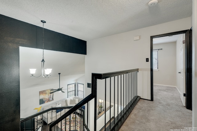 hall featuring an inviting chandelier, light carpet, and a textured ceiling