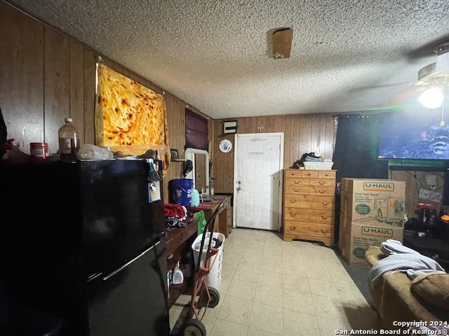 interior space with a textured ceiling, wood walls, light tile patterned floors, and black refrigerator