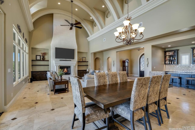 dining area featuring arched walkways, a high ceiling, built in shelves, a fireplace, and ceiling fan with notable chandelier