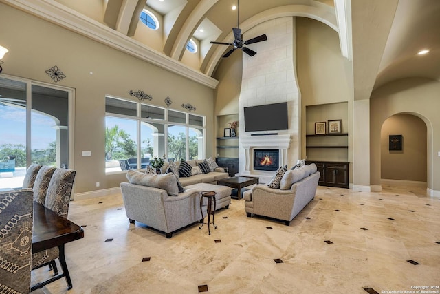 living room featuring built in features, a fireplace, a high ceiling, ceiling fan, and baseboards