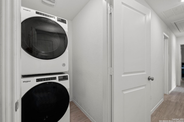 clothes washing area with light hardwood / wood-style flooring and stacked washer / drying machine