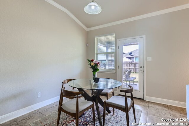 tiled dining room with ornamental molding and lofted ceiling