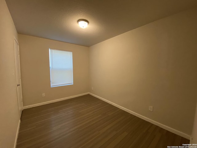 empty room featuring dark wood finished floors, a textured ceiling, and baseboards