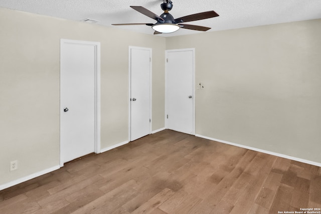 interior space with a textured ceiling, ceiling fan, two closets, and wood-type flooring